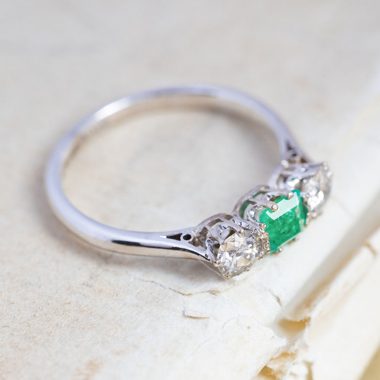 An antique, Art Deco emerald and old-cut diamond three-stone ring in white gold and platinum with a claw-set open back setting.
