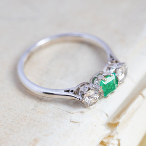 An antique, Art Deco emerald and old-cut diamond three-stone ring in white gold and platinum with a claw-set open back setting.