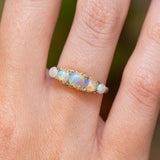 A close-up of an antique, Edwardian opal and diamond half-hoop ring in yellow gold. worn on a hand.