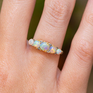 A close-up of an antique, Edwardian opal and diamond half-hoop ring in yellow gold. worn on a hand.