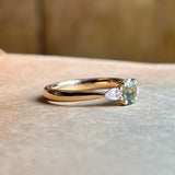 Sapphire and diamond three-stone engagement ring displayed on a book, showcasing elegance and sparkle.