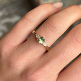 The three-stone sapphire engagement ring, greeny-teal sapphire, oval-cut sapphire ring, diamond accent ring being shown on the hand, unique engagement jewellery, luxury sapphire ring, sustainable gemstone ring