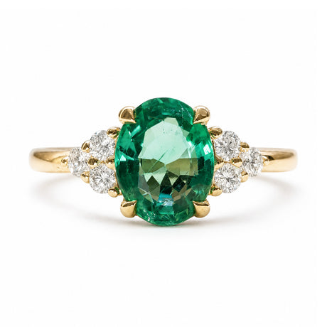 A vintage-inspired, oval-cut emerald and diamond cluster tre-foil engagement ring in yellow gold.
