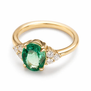 A three-quarter top view of a vintage-inspired, emerald and diamond tre-foil engagement ring.