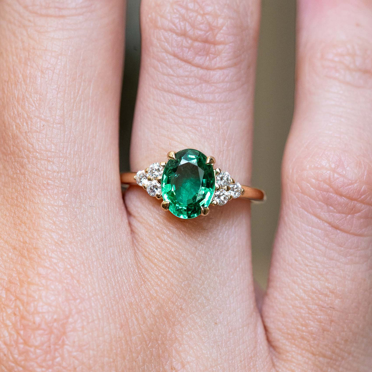 A vintage-inspired oval-cut emerald and diamond trefoil engagement ring in yellow gold worn on the finger.