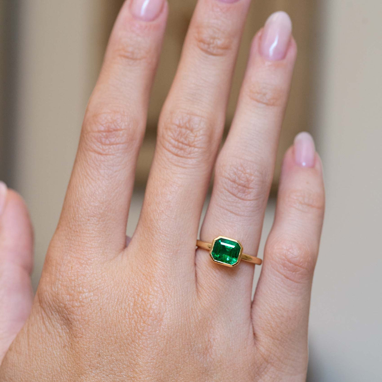 An antique-inspired emerald-cut emerald solitaire engagement ring worn on the hand.