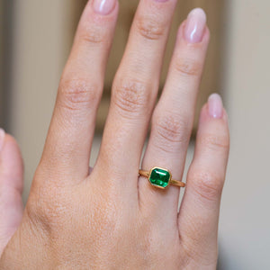 An antique-inspired emerald-cut emerald solitaire engagement ring worn on the hand.