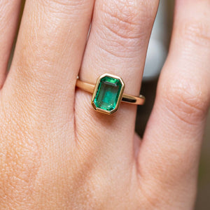 Emerald-cut emerald solitaire engagement ring in yellow gold with an antique-inspired design, worn on the finger.