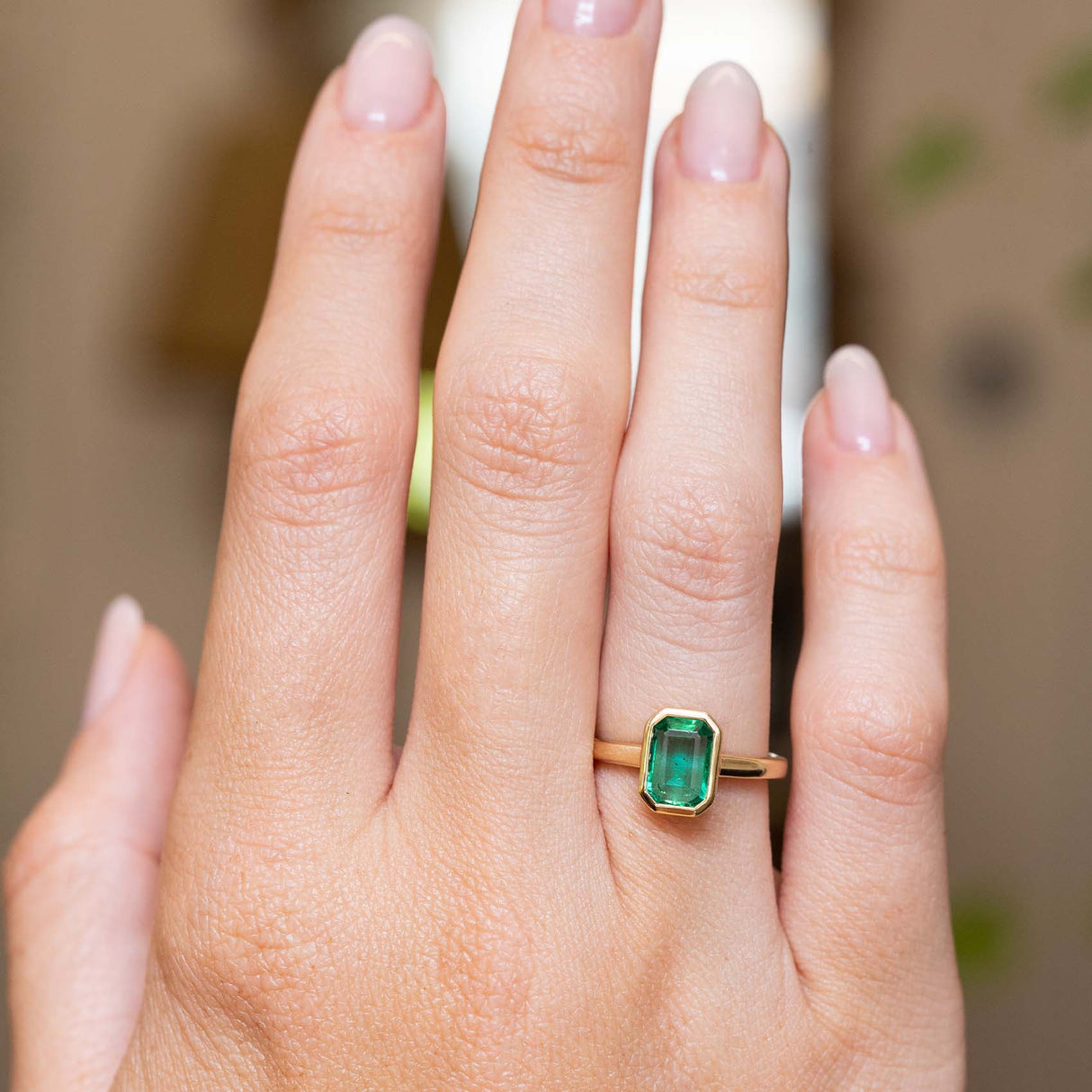 An emerald-cut emerald engagement ring in yellow gold showcased on the hand with an antique-inspired setting.