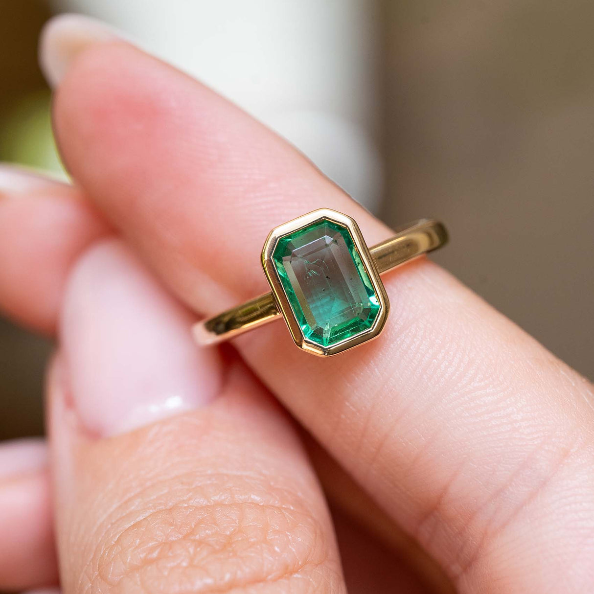 Close-up of an antique-inspired emerald-cut emerald solitaire engagement ring in yellow gold.