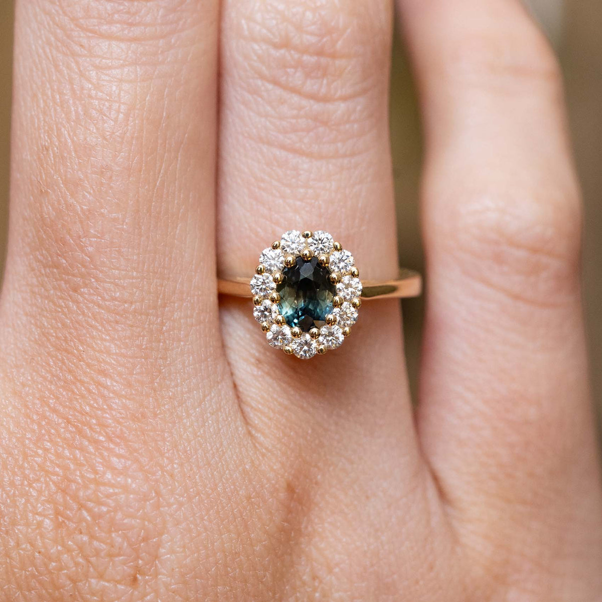 Antique-inspired deep green sapphire and diamond cluster engagement ring in yellow gold worn on the finger.