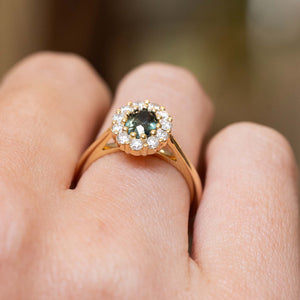 Close detail of an antique-inspired deep green sapphire surrounded by a brilliant diamond cluster in yellow gold.