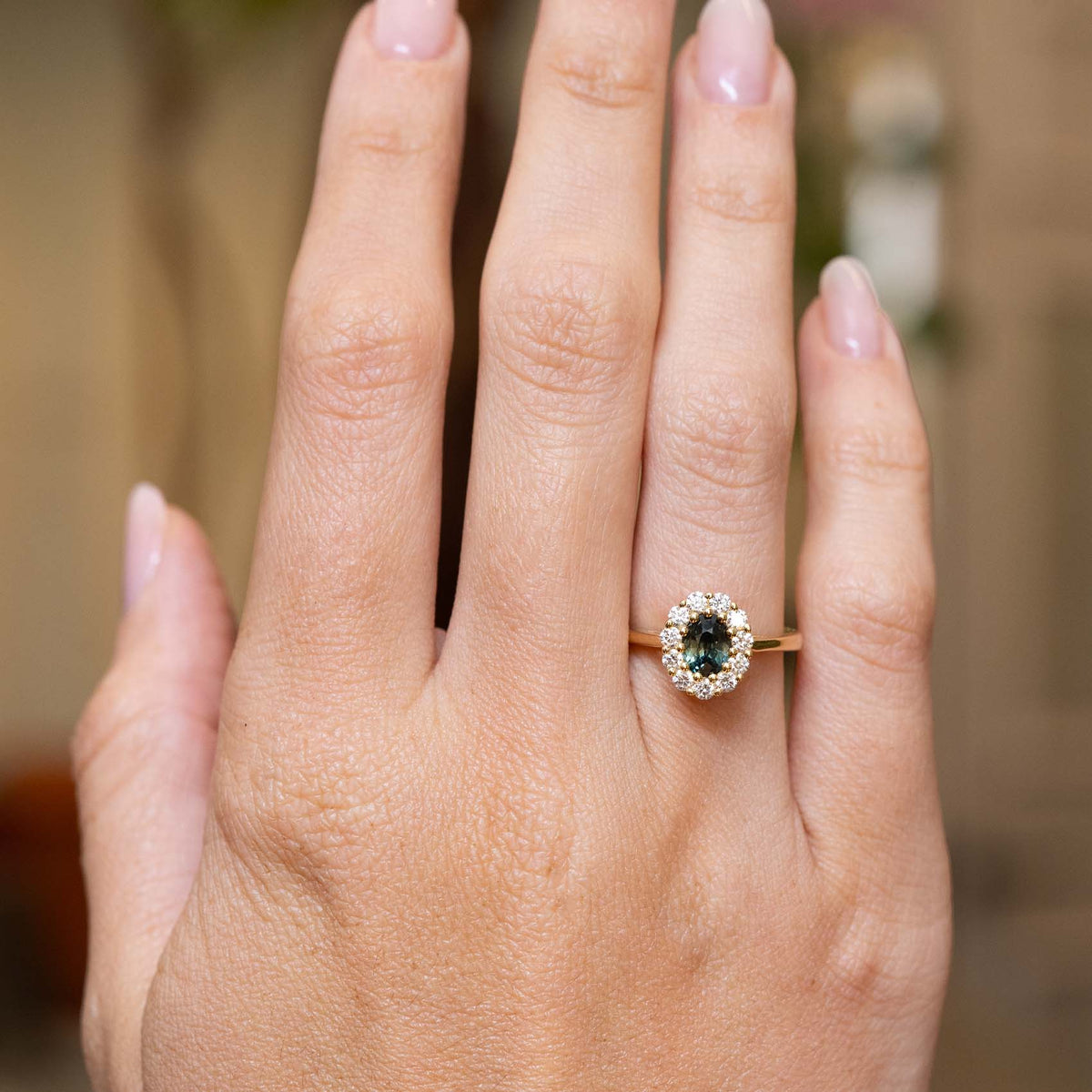 Deep green sapphire and diamond cluster engagement ring in yellow gold displayed on the hand.