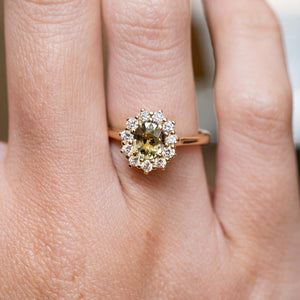 Antique-inspired green sapphire and diamond cluster engagement ring in yellow gold worn on the finger.