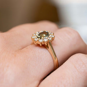 Close detail of a green sapphire surrounded by a sparkling diamond cluster in an antique-inspired yellow gold setting.
