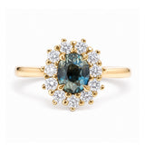 An antique-inspired, teal sapphire and diamond halo cluster engagement ring in yellow gold.