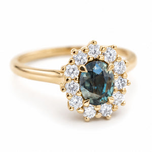 A vintage-inspired, blue-green sapphire and diamond halo engagement ring in 14ct yellow gold.
