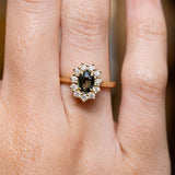 Antique-inspired green sapphire and diamond cluster engagement ring in yellow gold worn on the finger.