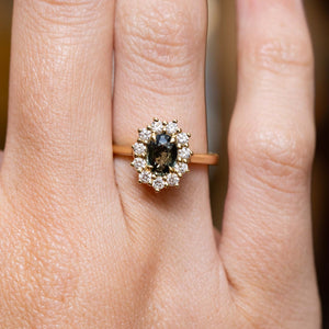 Antique-inspired green sapphire and diamond cluster engagement ring in yellow gold worn on the finger.