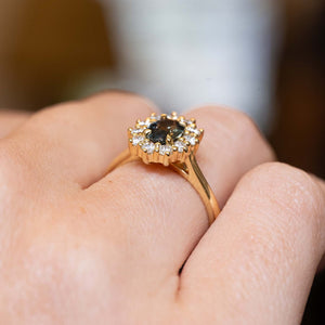 Close detail of a green sapphire engagement ring with a diamond halo in an antique-inspired yellow gold setting.