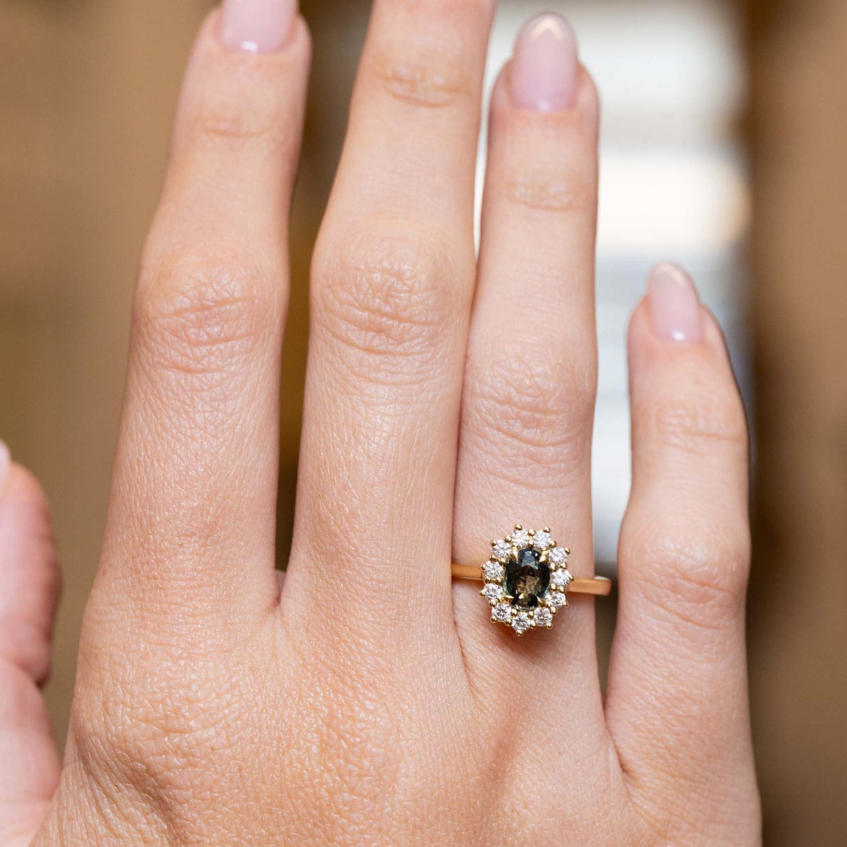 Green sapphire and diamond cluster engagement ring displayed on the hand in yellow gold.