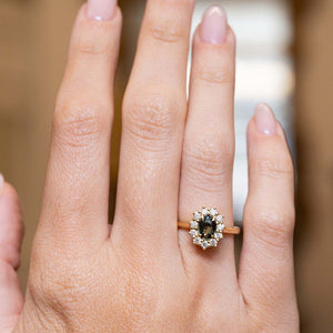 Green sapphire and diamond cluster engagement ring displayed on the hand in yellow gold.