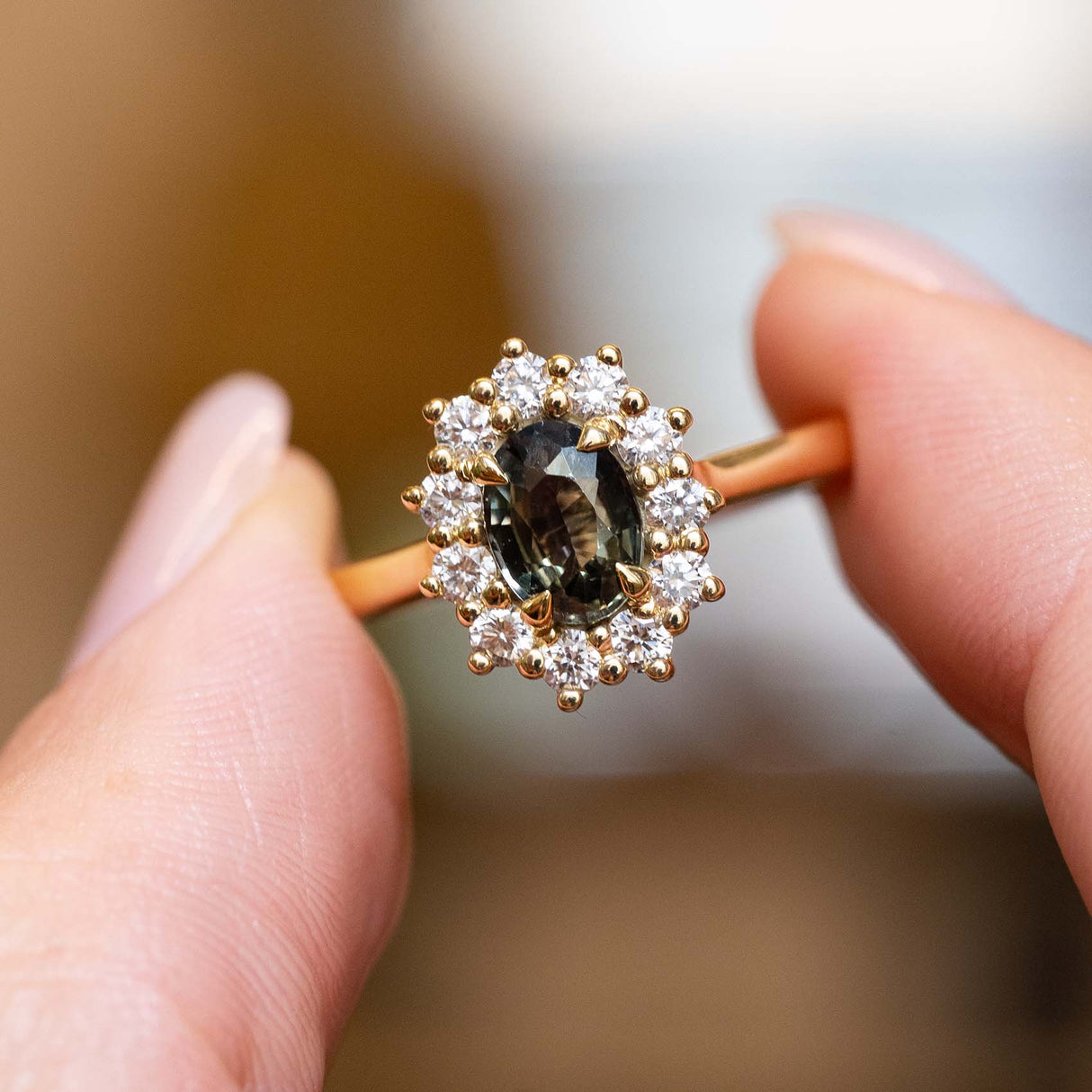 Close-up of an antique-inspired yellow gold engagement ring featuring a green sapphire surrounded by a diamond cluster.