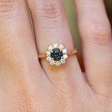 An antique-inspired dark teal sapphire and diamond cluster engagement ring worn on the finger.