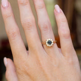 An antique-inspired dark teal sapphire and diamond cluster engagement ring worn on the hand.