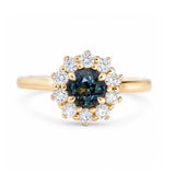 A close-up of an antique-inspired dark teal sapphire and diamond cluster engagement ring in 14ct yellow gold. 