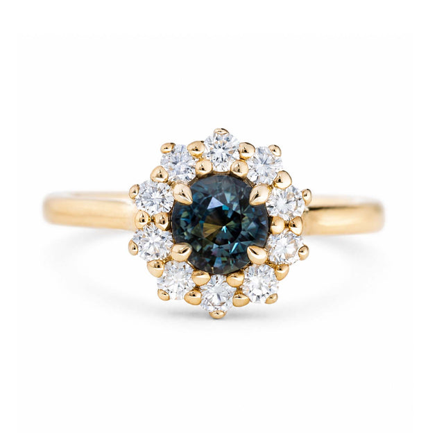 A close-up of an antique-inspired dark teal sapphire and diamond cluster engagement ring in 14ct yellow gold. 