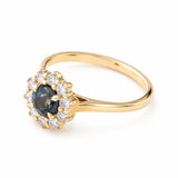A three-quarter of an vintage-inspired dark teal sapphire and diamond halo engagement ring in 14ct yellow gold. 