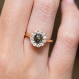 Antique-inspired earthy green sapphire and diamond cluster engagement ring in yellow gold worn on the finger. 