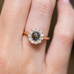 Antique-inspired earthy green sapphire and diamond cluster engagement ring in yellow gold worn on the finger. 