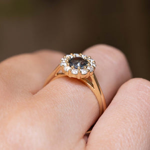 Close detail of an antique-inspired earthy green sapphire halo engagement ring with a diamond cluster in yellow gold.