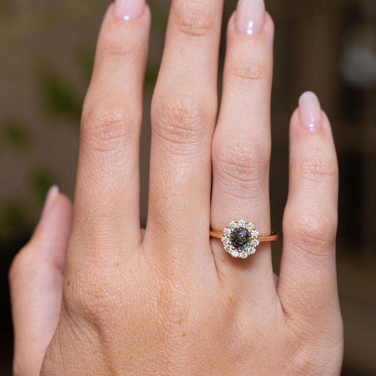 Earthy green sapphire and diamond engagement ring displayed on the hand in an antique-inspired yellow gold setting.