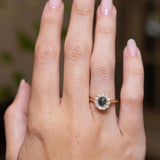 Earthy green sapphire and diamond engagement ring displayed on the hand in an antique-inspired yellow gold setting.