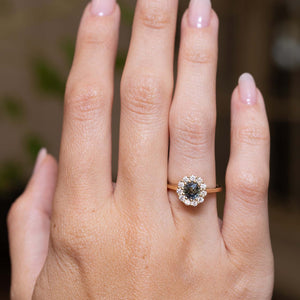 Earthy green sapphire and diamond engagement ring displayed on the hand in an antique-inspired yellow gold setting.