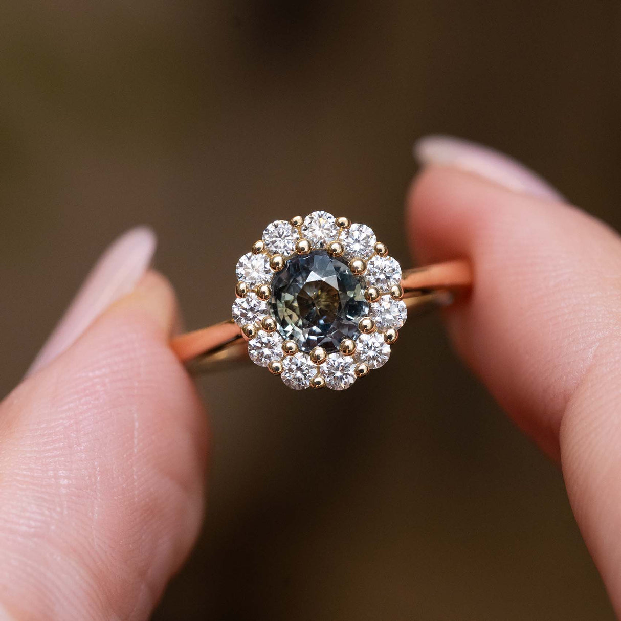 Close-up of an antique-inspired yellow gold ring featuring an earthy green sapphire surrounded by a diamond cluster.