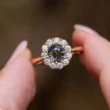Close-up of an antique-inspired yellow gold ring featuring an earthy green sapphire surrounded by a diamond cluster.