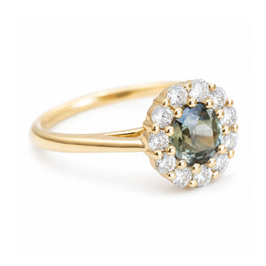 A vintage-inspired yellow gold ring with a central green-blue gemstone and diamond halo on a book.