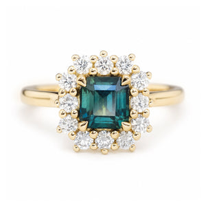A close-up photo of an antique-inspired, teal sapphire and diamond cluster engagement ring in yellow gold.