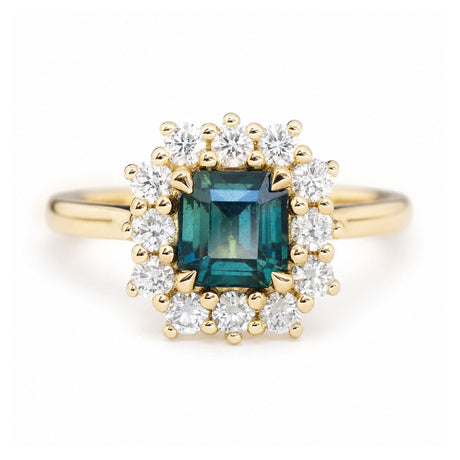 A close-up photo of an antique-inspired, teal sapphire and diamond cluster engagement ring in yellow gold.