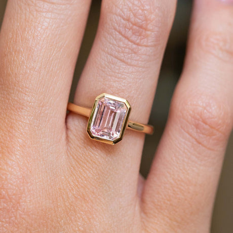 A close-up of an antique inspired, soft petal-pink sapphire solitaire engagement ring in yellow gold. 