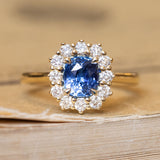 An antique-inspired, blue sapphire and diamond cluster engagement ring in yellow gold.