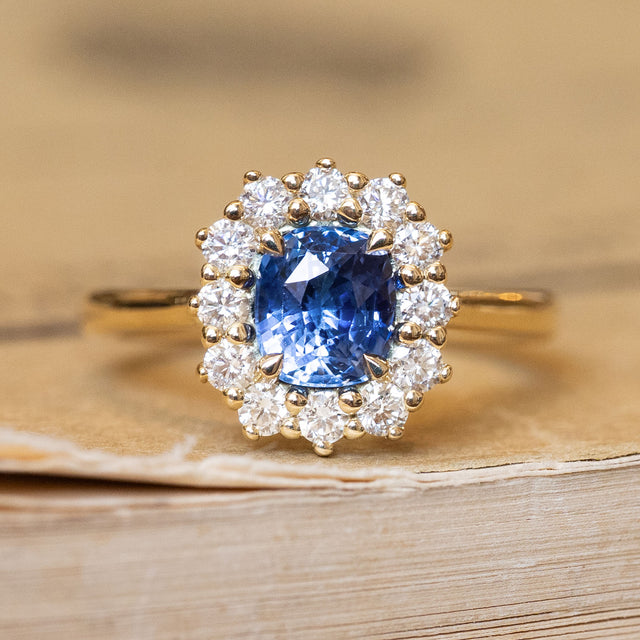 An antique-inspired, blue sapphire and diamond cluster engagement ring in yellow gold.