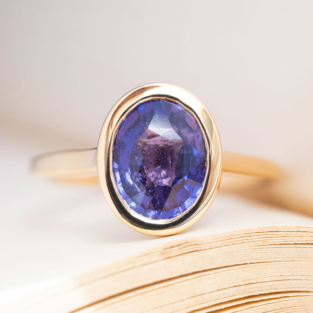 An antique-inspired, royal purple oval sapphire solitaire ring in 14ct yellow gold.