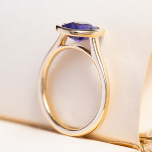 A vintage-inspired, royal purple oval sapphire solitaire ring in 14ct yellow gold with a minimalist open-back setting.