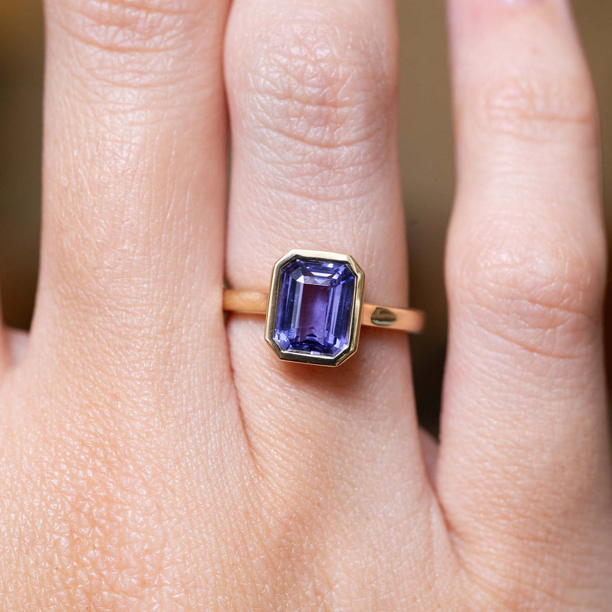 Antique-inspired indigo blue sapphire solitaire engagement ring in yellow gold worn on the finger.