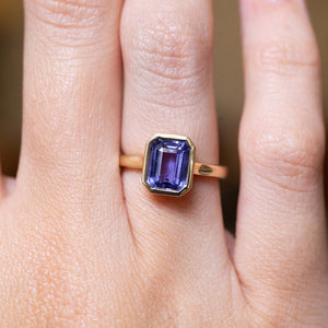 Antique-inspired indigo blue sapphire solitaire engagement ring in yellow gold worn on the finger.